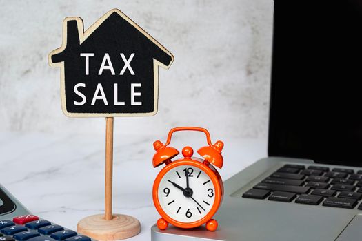 Tax Sale text on wooden house model with notebook and calculator on white table. Real estate property tax concept.