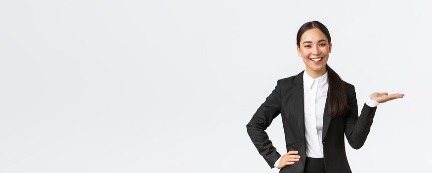 Professional smiling businesswoman introduce her project during meeting. Saleswoman in black suit holding hand right as showing product, holding on palm over blank white background.