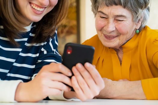 Young girl, a granddaughter, explains to an elderly relative how to use a smartphone and an application to communicate with a doctor at home. The family loves and cares for their elderly parents.