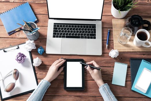 Business woman working at office desk. Flat lay wooden desk with laptop and tablet computer with white blank screen. Top view office workplace with woman hands. Online business and internet commerce