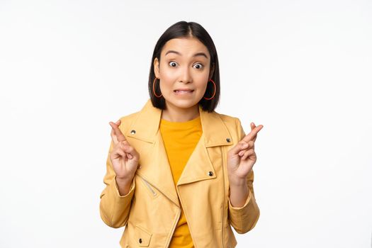 Portrait of excited asian woman looks hopeful, wishing, praying or begging, waiting for news, standing over white background, smiling enthusiastic.