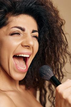 Overjoyed pretty adorable tanned sexy curly Latin makeup artist hold brush like micro singing relaxing satisfied posing isolated on pastel beige background close eyes. Cosmetic offer concept closeup