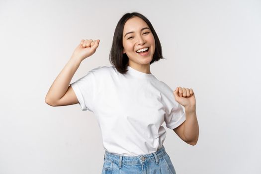 Happy dancing korean girl posing against white background, wearing tshirt.