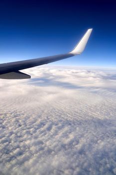 View of airplane wing on blue sky background. Plane over clouds in the sky.