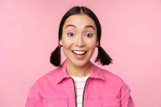 Close up portrait of beautiful asian girl looking enthusiastic and smiling, laughing and smiling, standing happy against pink background.