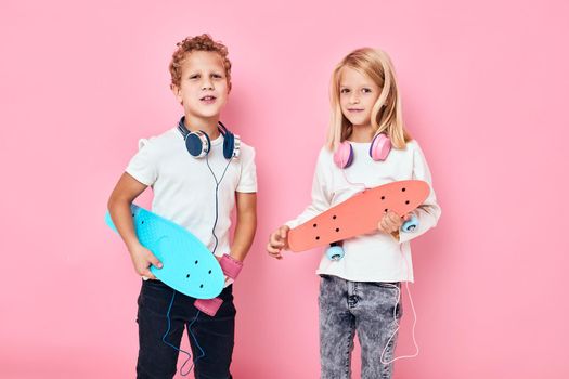 Stylish little boy and cute girl in headphones skateboards in hands isolated background. High quality photo