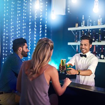 Shot of a happy bartender serving drinks to a couple in a nightclub.
