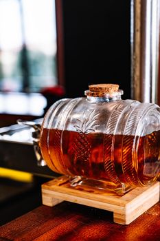 detail shot of a small transparent glass barrel with amber coloured sweet wine. Warm and dim light.