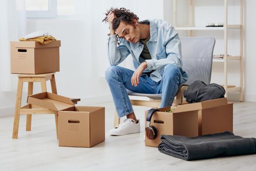 guy with curly hair sitting on a chair unpacking with box in hand moving Lifestyle. High quality photo