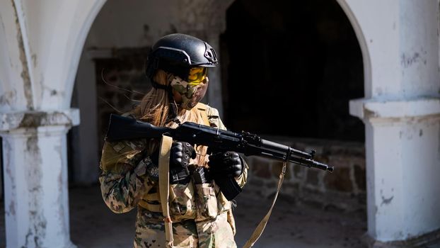 Caucasian woman in a protective suit with a machine gun. FA female soldier in a camouflage uniform holds a weapon