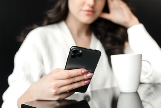 Portrait of an attractive young woman browsing social media or news in a coffee shop. A young woman looks into the phone and holds a mug of coffee. Close up.
