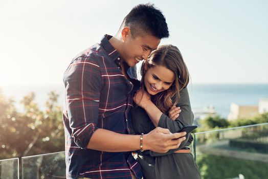 Shot of an affectionate young couple using a cellphone together while relaxing outdoors.