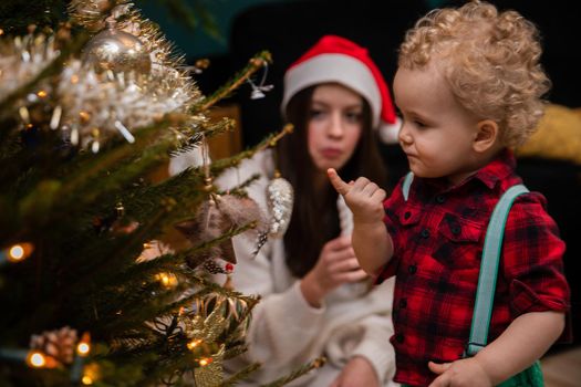 Siblings while decorating a Christmas tree. A two-year-old child with curly blonde hair and a teenage brunette as brother and sister.