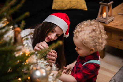 A teenage girl and her brother decorate a Christmas tree for Christmas. A two-year-old child with curly blonde hair.