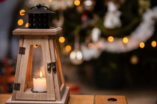 The peaceful flame of a burning candle against a background of fuzzy Christmas tree lights. Christmas atmosphere of the holidays in December.