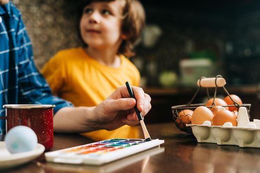 Easter day. Male Father and son painting eggs on wooden background. Family sitting in a kitchen. Preparing for Easter, creative homemade decoration. Child kid boy having fun and painting easter eggs