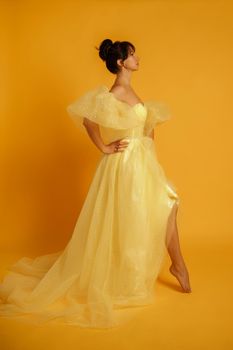 Profile portrait of a beautiful middle-aged woman in a yellow dress, her hair pulled up against a yellow background.