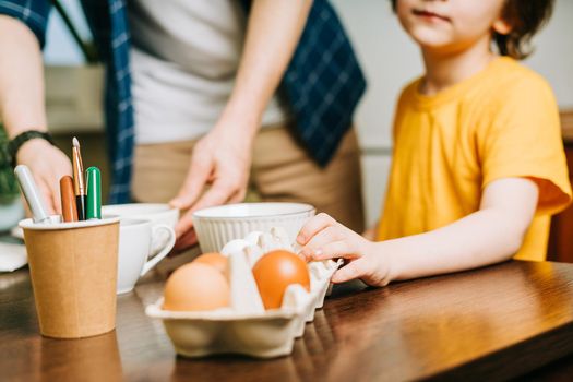 Easter day. Male Father and son painting eggs on wooden background. Family sitting in a kitchen. Preparing for Easter, creative homemade decoration. Child kid boy having fun and painting easter eggs