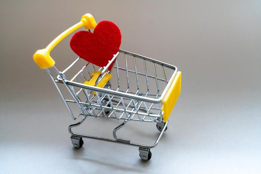 Shopping basket on a gray background with a bright red heart. Close-up