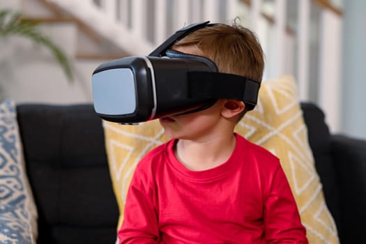 Happy caucasian boy sitting on sofa, wearing vr headset, having fun. childhood, leisure and discovery using technology at home.