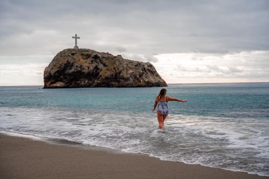 A plump woman in a bathing suit enters the water during the surf. Alone on the beach, Gray sky in the clouds, swimming in winter