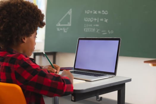 African american schoolboy sitting at desk in classroom using laptop, with copy space on screen. childhood, technology and education at elementary school.