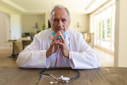 Senior caucasian male doctor wearing face mask having a video call. medicine and healthcare services during covid 19 pandemic concept.