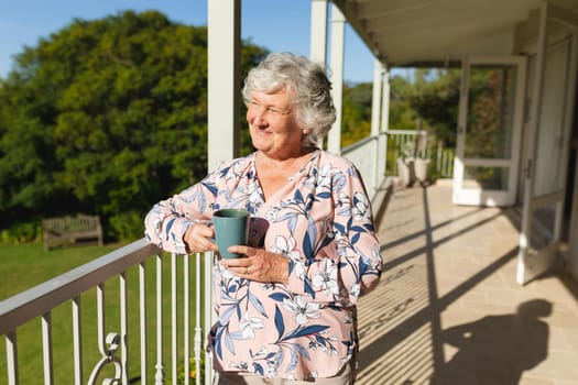 Senior caucasian woman standing on balcony holding mug and smiling. retreat, retirement and happy senior lifestyle concept.