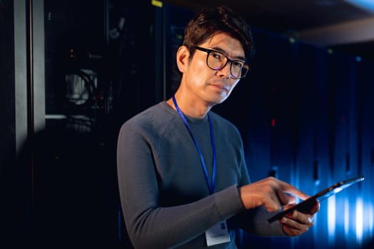 Portrait of asian male engineer using digital tablet in computer server room. database server management and maintenance concept