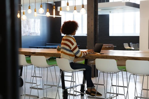 Mixed race businesswoman sitting at conference table with laptop and having video call. independent creative design business.