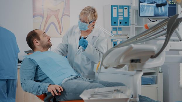 Patient with mouth open receiving examination from dentist at oral care clinic, using dental instruments. Orthodontist consulting man with toothache for dentistry diagnosis. Dentition work