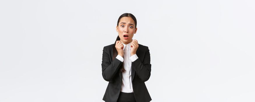 Worried and shocked asian female entrepreneur in suit hear worrying news, holding hands near face and gasping concerned, looking in panic. Businesswoman have trouble, awful problem.