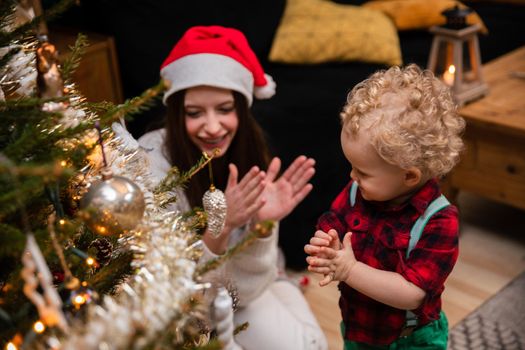 The joy and applause of a sister and brother for a wonderfully decorated Christmas tree. A two-year-old child with curly blonde hair and a teenage brunette as brother and sister.