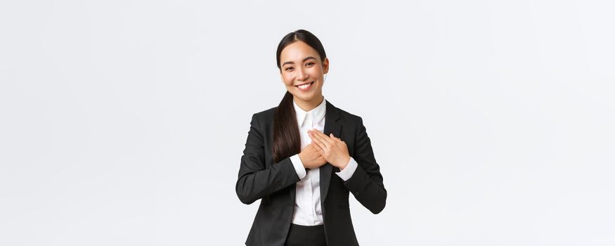 Happy pleased asian female entrepreneur love her clients, feeling flattered as receive praises with great job, holding hands on heart and smiling thankful, being grateful and appreciate efforts.