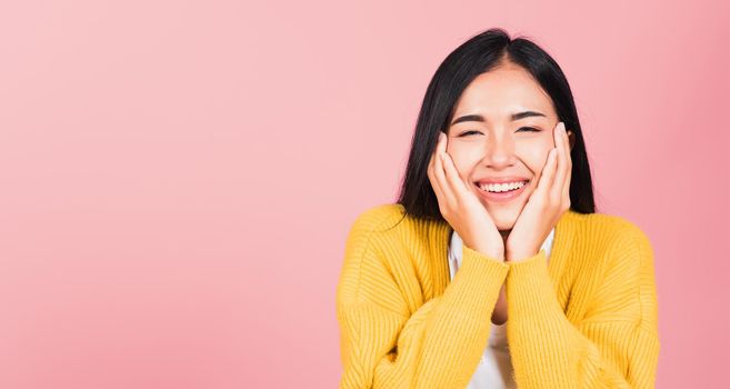 Happy Asian portrait beautiful cute young woman smile holding her cheeks looking to camera studio shot isolated on pink background Thai female beauty face touch massage healthy skin with copy space