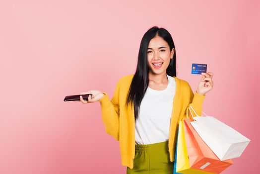 Portrait Asian happy beautiful young woman shopper smiling standing excited holding online shopping bags colorful and credit card for payment on hand in summer, studio shot isolated on pink background