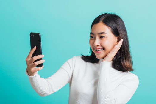 Beautiful Asian woman smile she using a smartphone to selfie photo, happy female photography by mobile phone on mobile phone isolated on a blue background, Technology concept