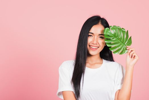 Beauty face. Portrait of Asian beautiful young woman with fresh healthy skin hold green monstera leaf on her face, Tropical Leaves, studio shot isolated on pink background, Skin body care spa concept