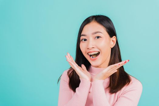 Happy young Asian beautiful woman smiling wear silicone orthodontic retainers on teeth surprised she is excited screaming and raise hand make gestures wow, studio shot isolated on blue background