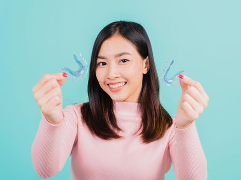 Portrait Asian beautiful young woman smiling hold silicone orthodontic retainers for teeth, Teeth retaining tools after removable braces, isolated blue background, Dental hygiene healthy care concept