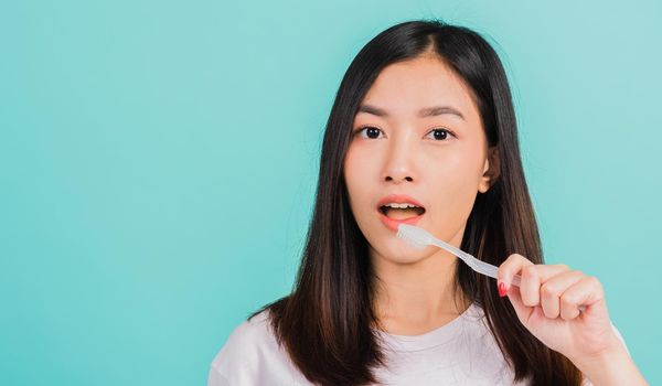 Asian beautiful young woman teen brushing teeth in the morning, portrait of happy Thai female confident smiling holding toothbrush, studio shot isolated on blue background, Dental health concept