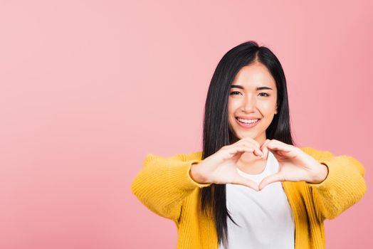 Happy Asian portrait beautiful cute young woman smile make finger heart gesture figure symbol shape sign with two hands sending love to her lover looking camera, studio shot isolated pink background