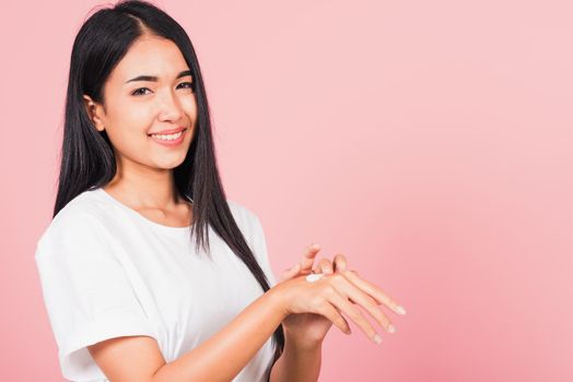 Portrait of Asian beautiful young woman applying lotion cosmetic moisturizer cream on her behind the palm skin back hand, studio shot isolated on pink background,  Hygiene skin body care concept