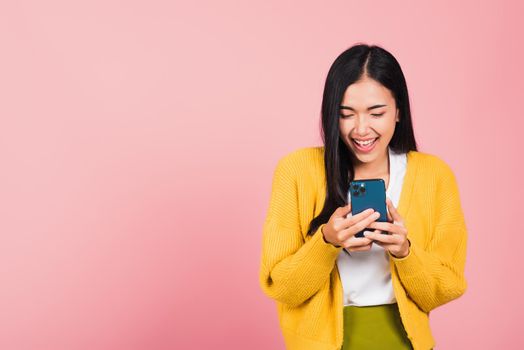 Happy Asian portrait beautiful cute young woman teen smiling excited using smart mobile phone studio shot isolated on pink background, Thai female surprised making winner gesture on smartphone