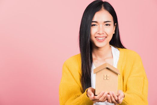 Happy Asian portrait beautiful cute young woman excited smiling holding house model on hand, studio shot isolated on pink background, broker female hold home real estate insurance and banking concept