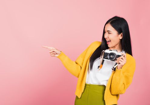 Attractive energetic happy Asian portrait beautiful cute young woman teen excited smiling holding vintage photo camera and pointing finger to side space, studio shot isolated on pink background