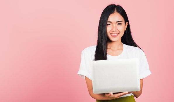 Portrait of happy Asian beautiful young woman confident smiling face holding using laptop computer looking to camera, studio shot isolated on pink background, with copy space