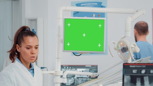Close up of dentist looking at monitor with green screen for teeth scan examination in dental office. Dentistry specialist using chroma key with mockup template and isolated background