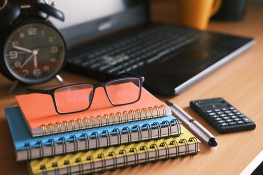 color notepads, eyeglass, clock and laptop on table .