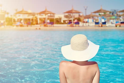 Woman in hat relaxing in swimming pool at water park. Summer holiday